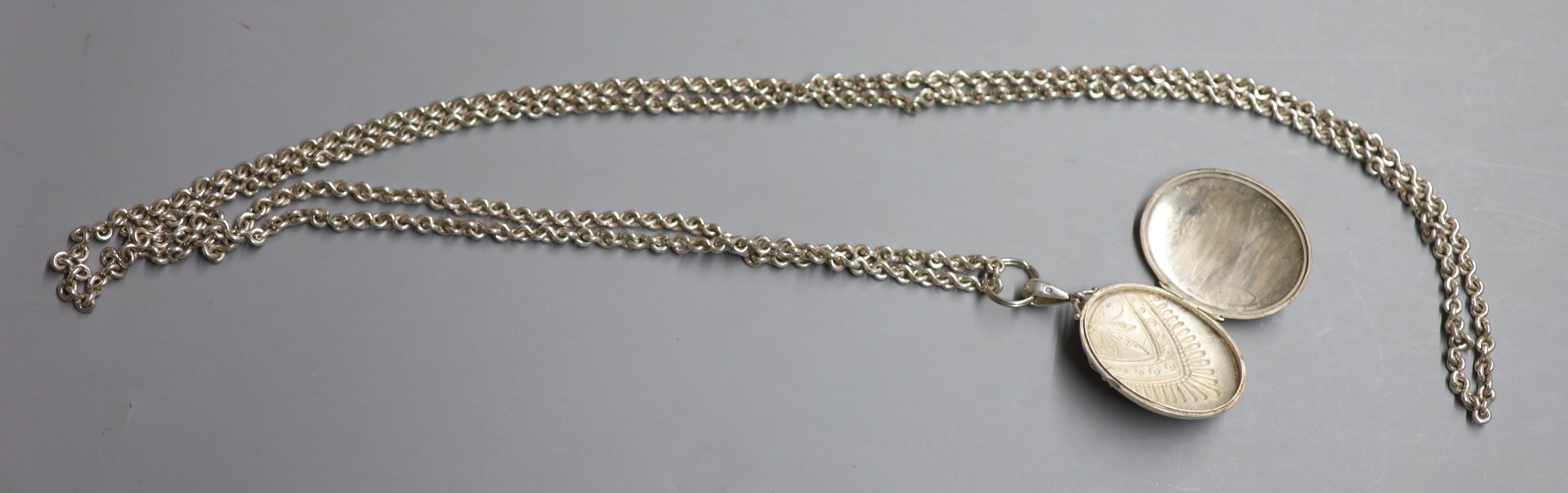 A late Victorian silver oval locket, 47mm, on a long white metal chain, 148cm, gross 124 grams.